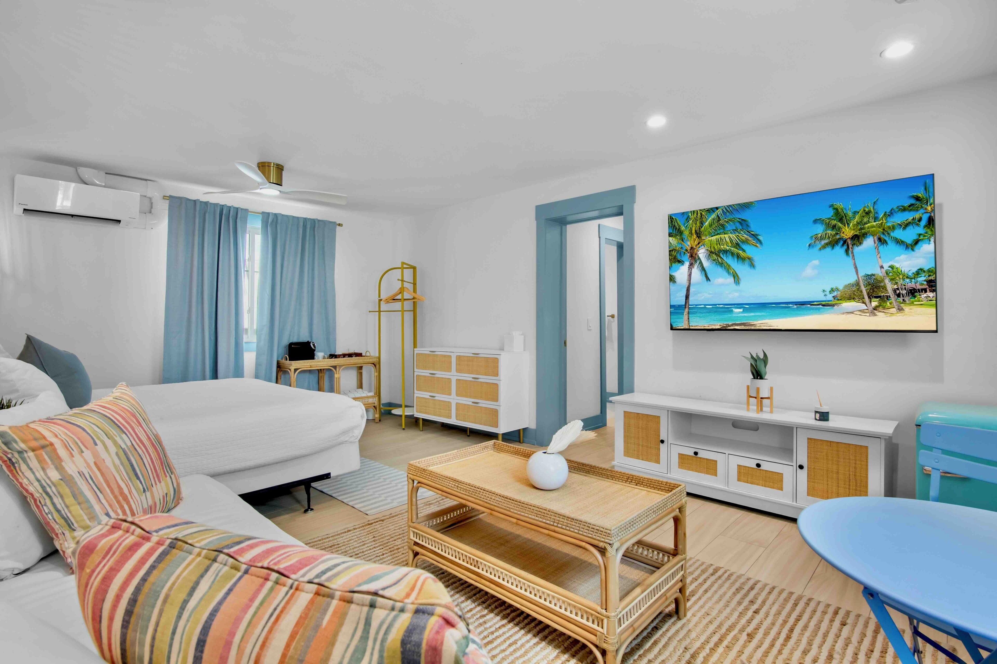 A hotel room with a bed, a sofa, a coffee table, a TV, and a painting of a beach scene.