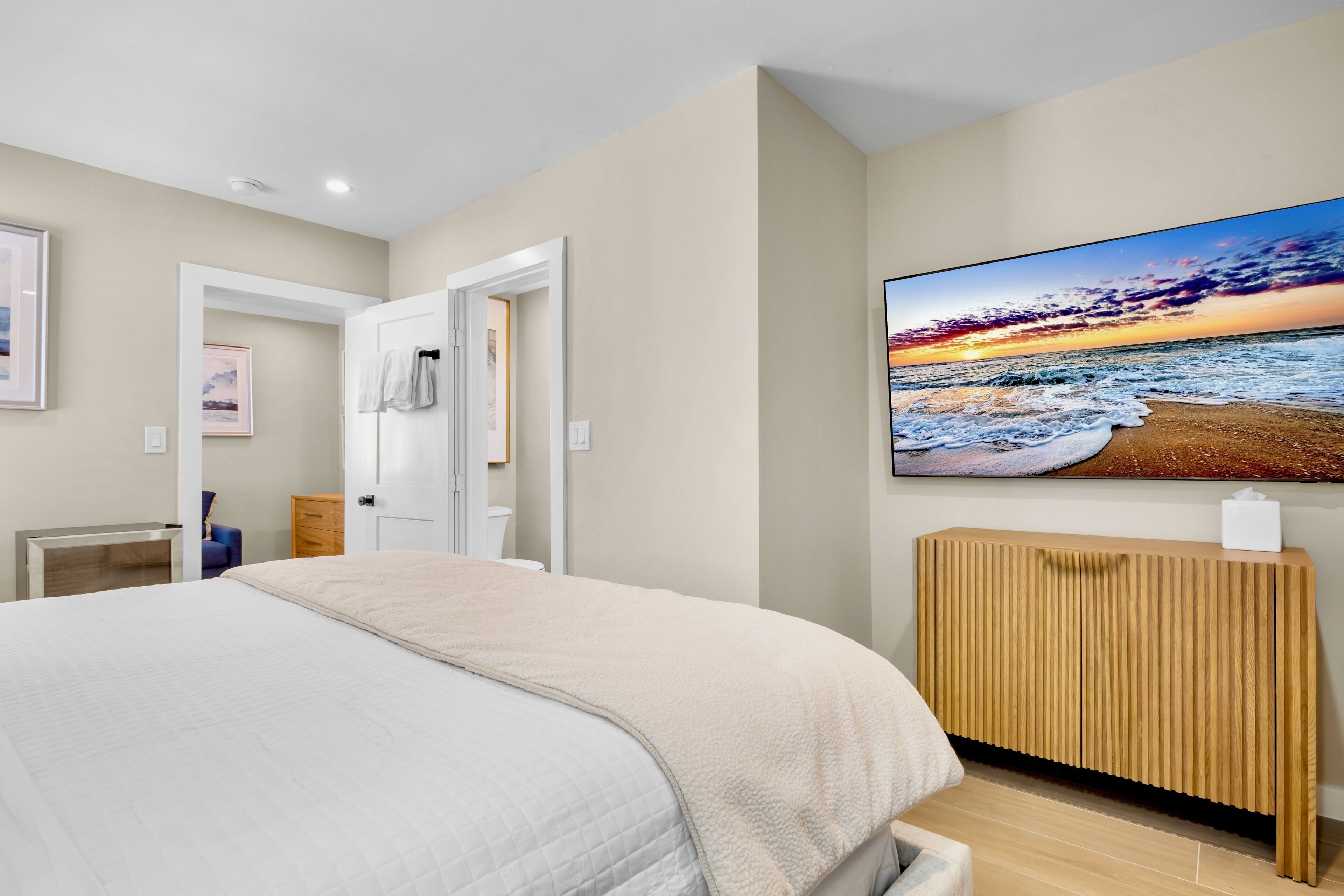 Une chambre à coucher comprenant un lit, une table de chevet en bois, un téléviseur fixé au mur et une porte donnant sur une autre pièce.