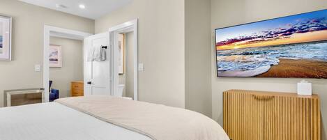 Une chambre à coucher comprenant un lit, une table de chevet en bois, un téléviseur fixé au mur et une porte donnant sur une autre pièce.