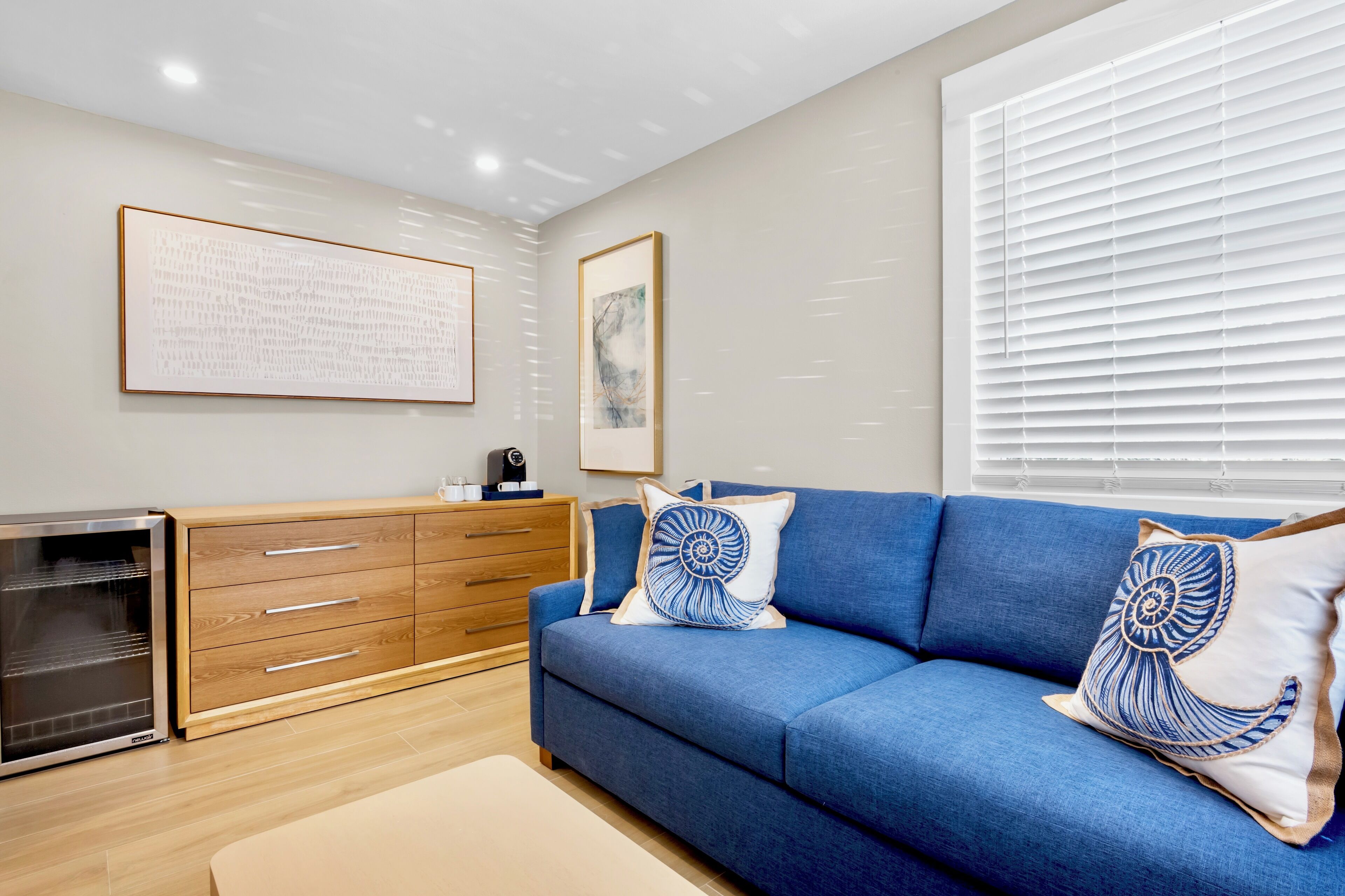 Una sala moderna con un sofá azul, un aparador de madera y un electrodoméstico con puerta de cristal.