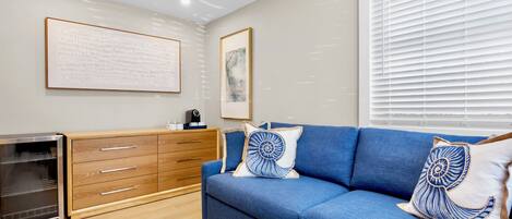 A modern living room with a blue sofa, wooden cabinet, and a glass-fronted appliance.