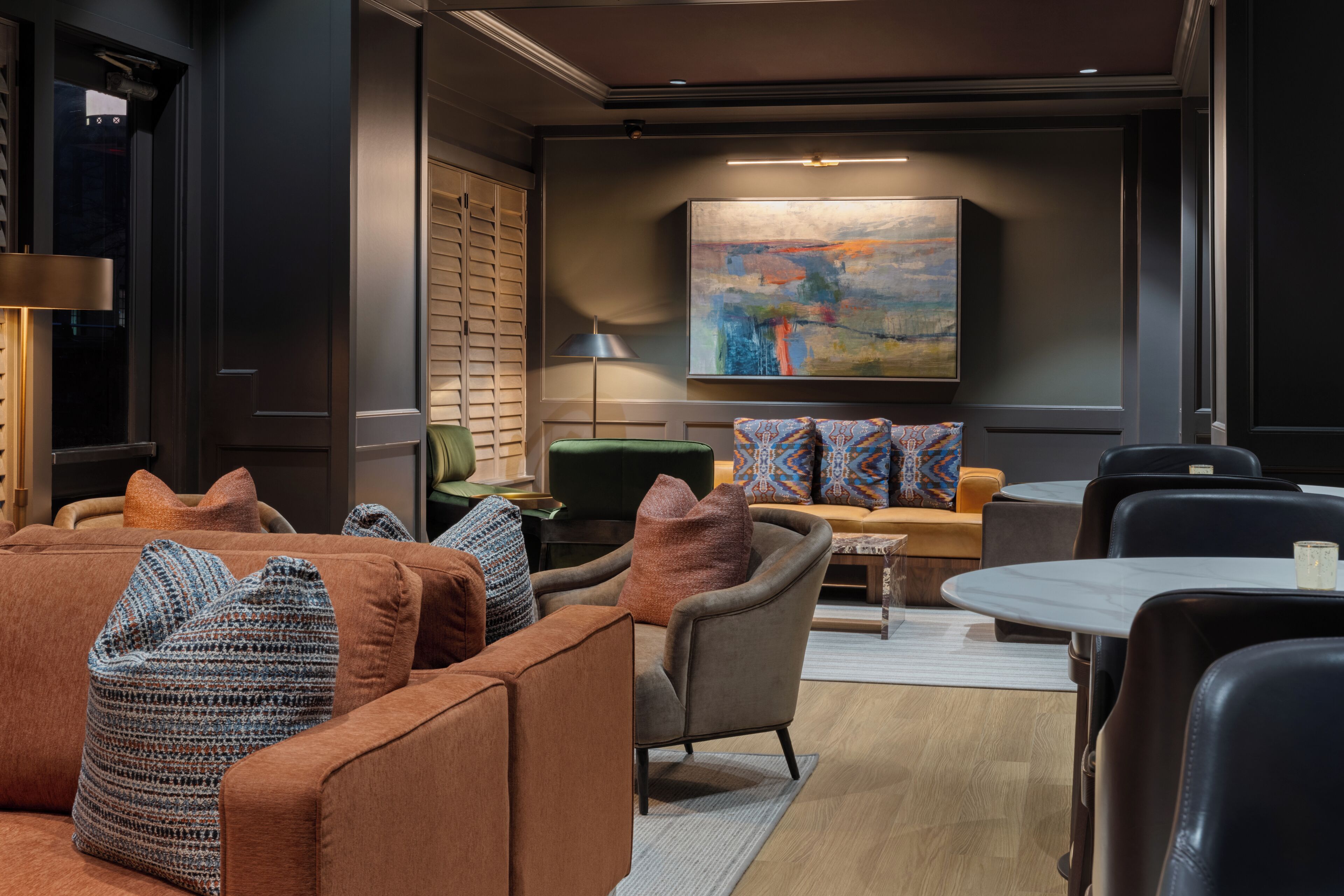 A modern lounge area with seating, a painting on the wall, and a lamp.