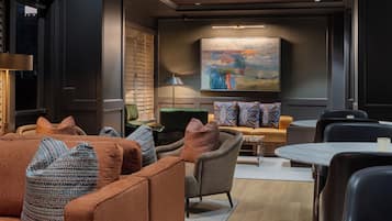A modern lounge area with seating, a painting on the wall, and a lamp.
