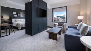 Une chambre d’hôtel moderne, dotée d’un grand lit, d’un canapé, d’un bureau et d’un téléviseur fixé au mur.