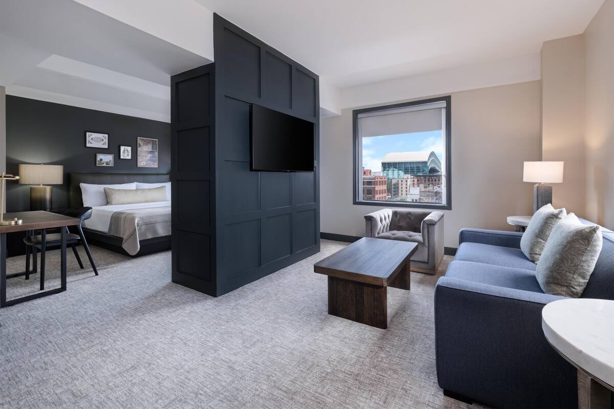 A modern hotel room with a large bed, a sofa, a desk, and a TV mounted on the wall.