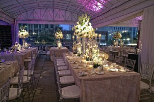 A banquet hall with long tables, clear chairs, and floral centerpieces.