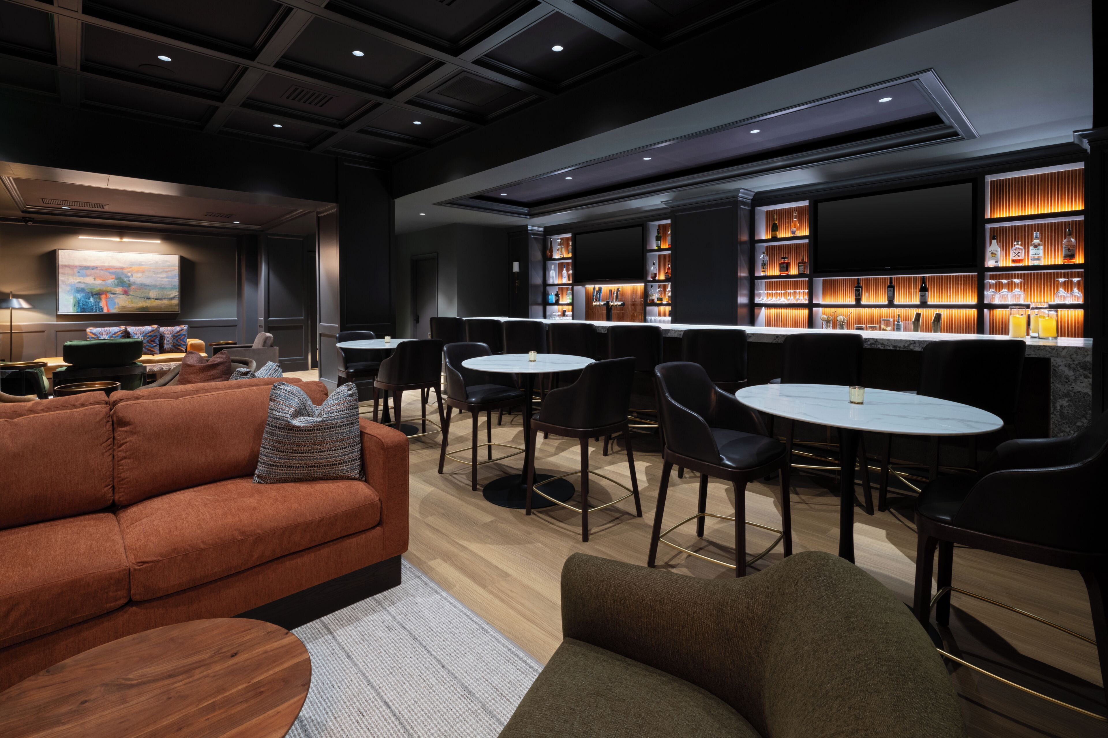A modern lounge area with sofas, chairs, and a bar with shelves of bottles.