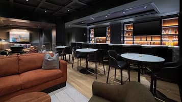 A modern lounge area with sofas, chairs, and a bar with shelves of bottles.