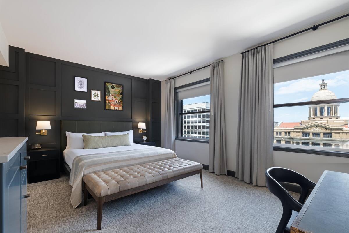 A hotel room with a large bed, a desk, and a view of a building with a dome through the window.