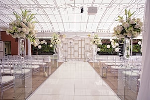 A wedding venue with a clear aisle, white floral arrangements, and a tiled floor.