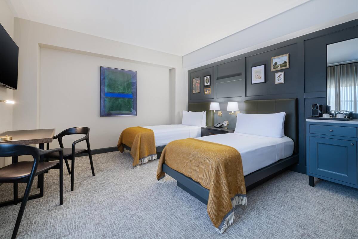 A hotel room with two beds, a desk, chairs, a TV, and a minibar.