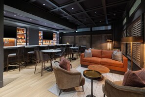 Un espace de détente moderne comprenant un canapé, des fauteuils, une table basse et un bar avec des étagères remplies de bouteilles.