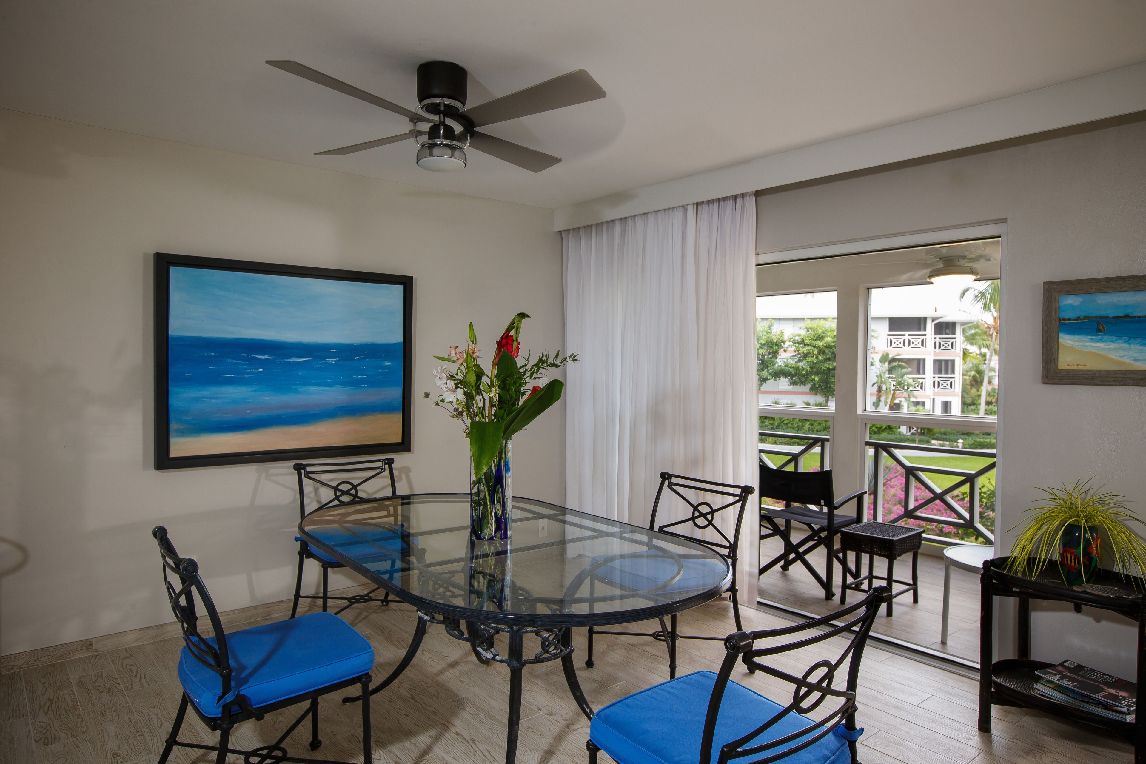 Un coin repas avec une table en verre, des chaises bleues et un ventilateur de plafond.