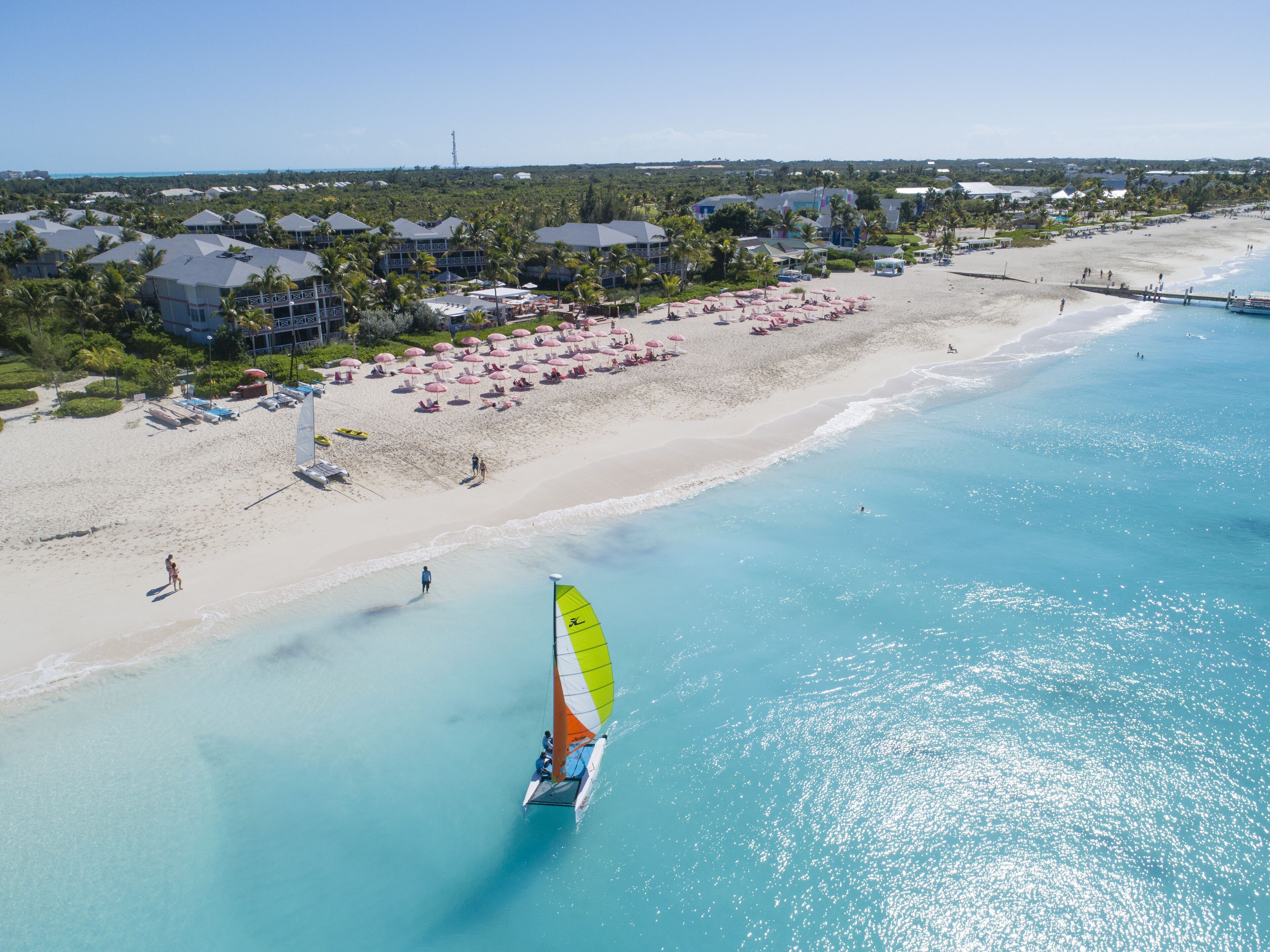 A beach resort with a clear view of the ocean, a sandy beach, and a sailboat.