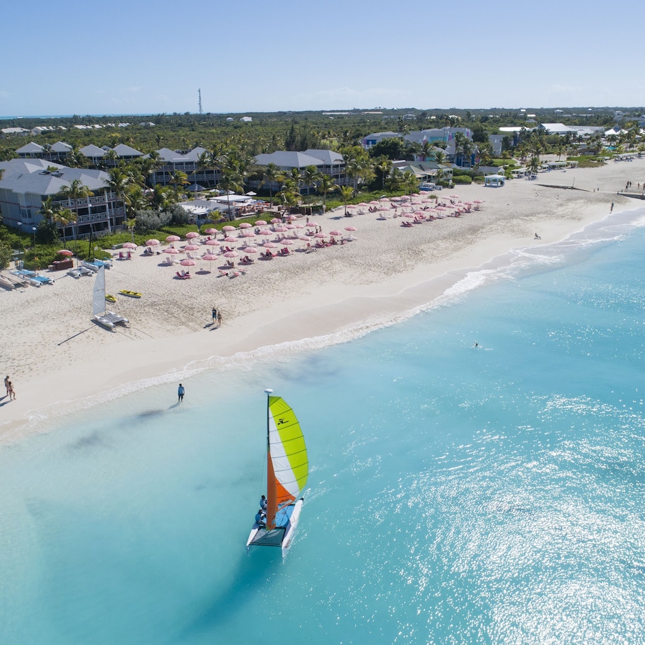 A beach resort with a clear view of the ocean, a sandy beach, and a sailboat.