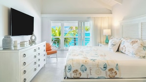 A bedroom with a large bed, a dresser, a TV, and a balcony with a view of the ocean. - Ocean Club East, Grace Bay Beach (Providenciales)