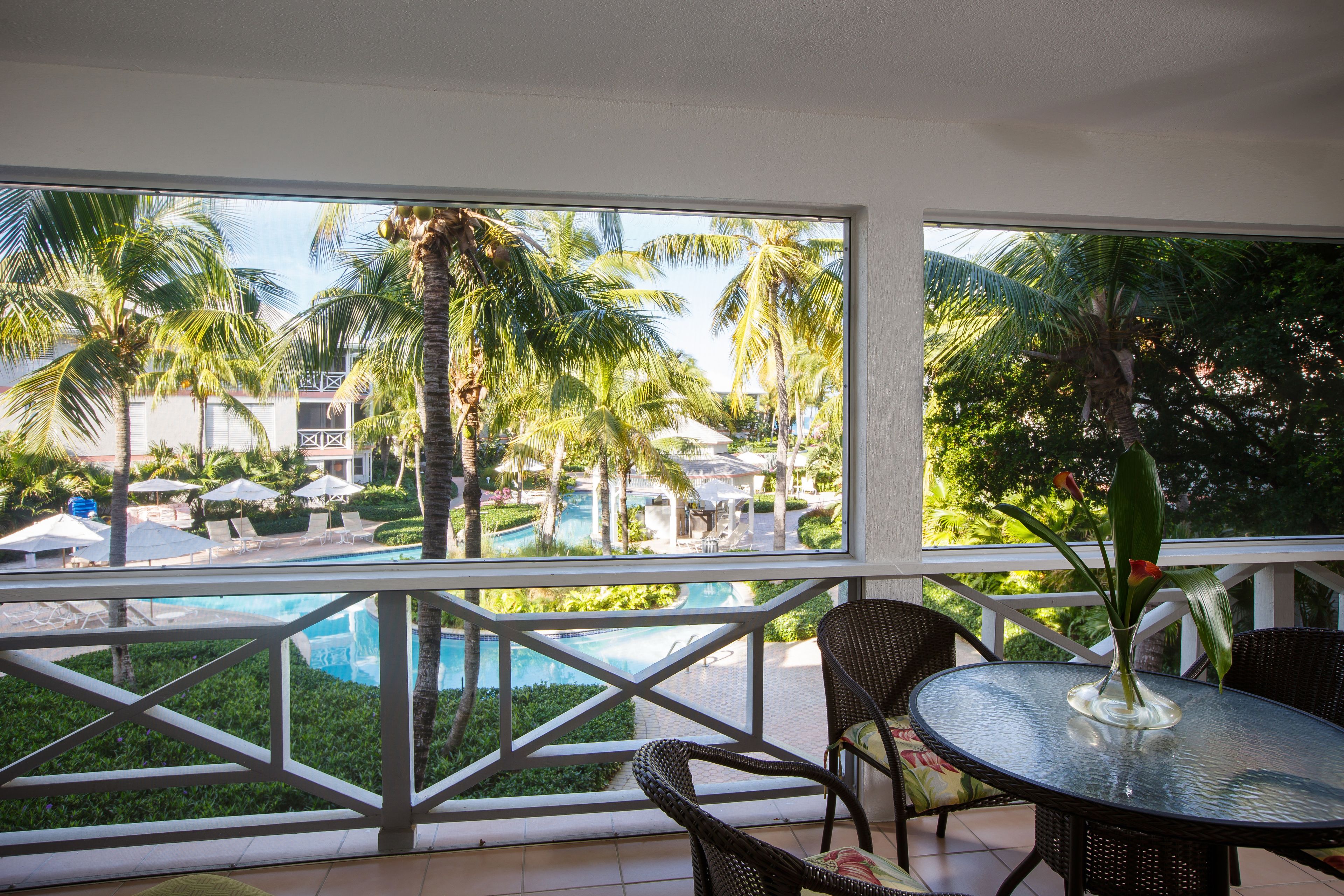 A balcony with a view of a swimming pool, palm trees, and lounge chairs.