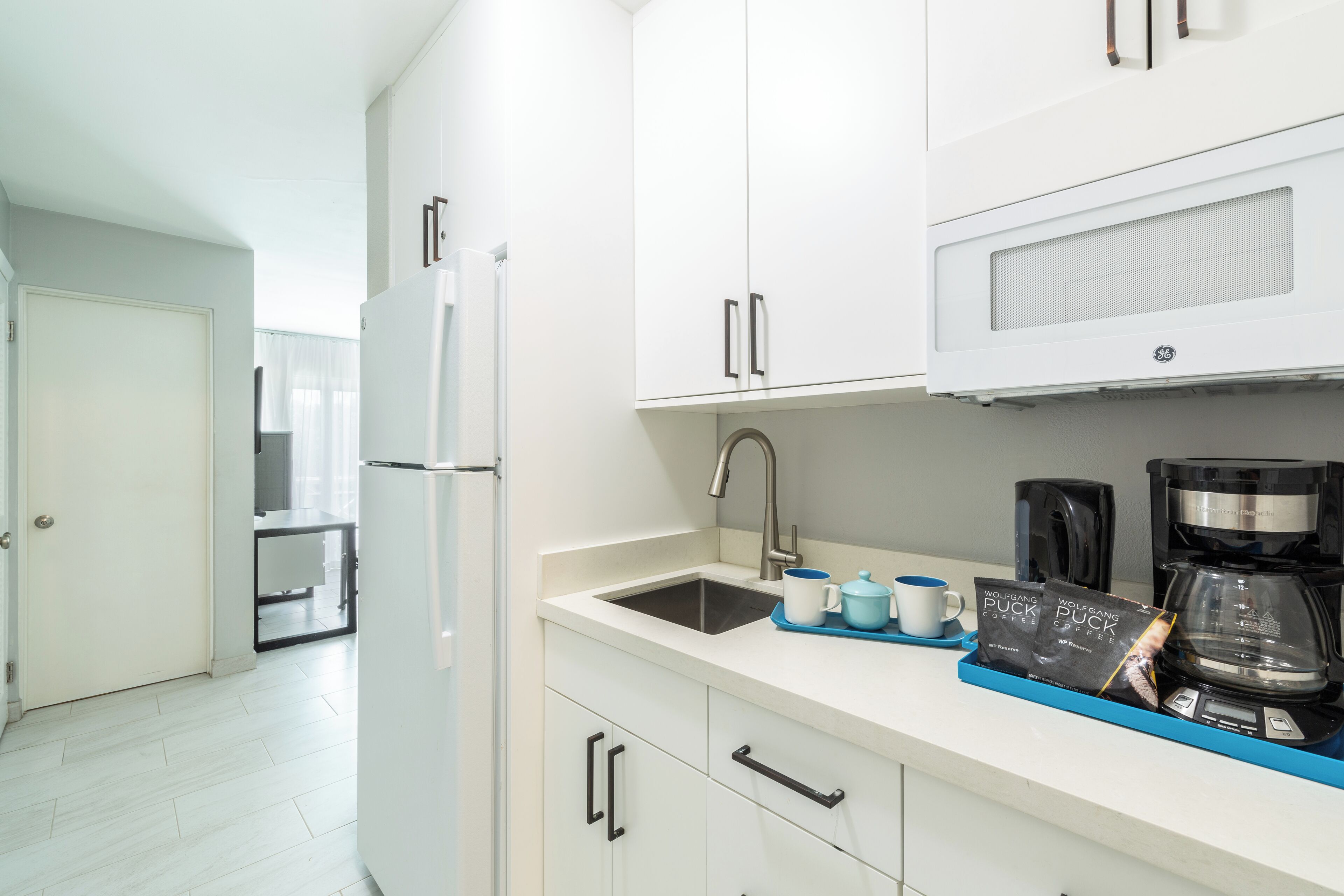 A modern kitchen with white cabinets, a built-in sink, and a coffee maker.