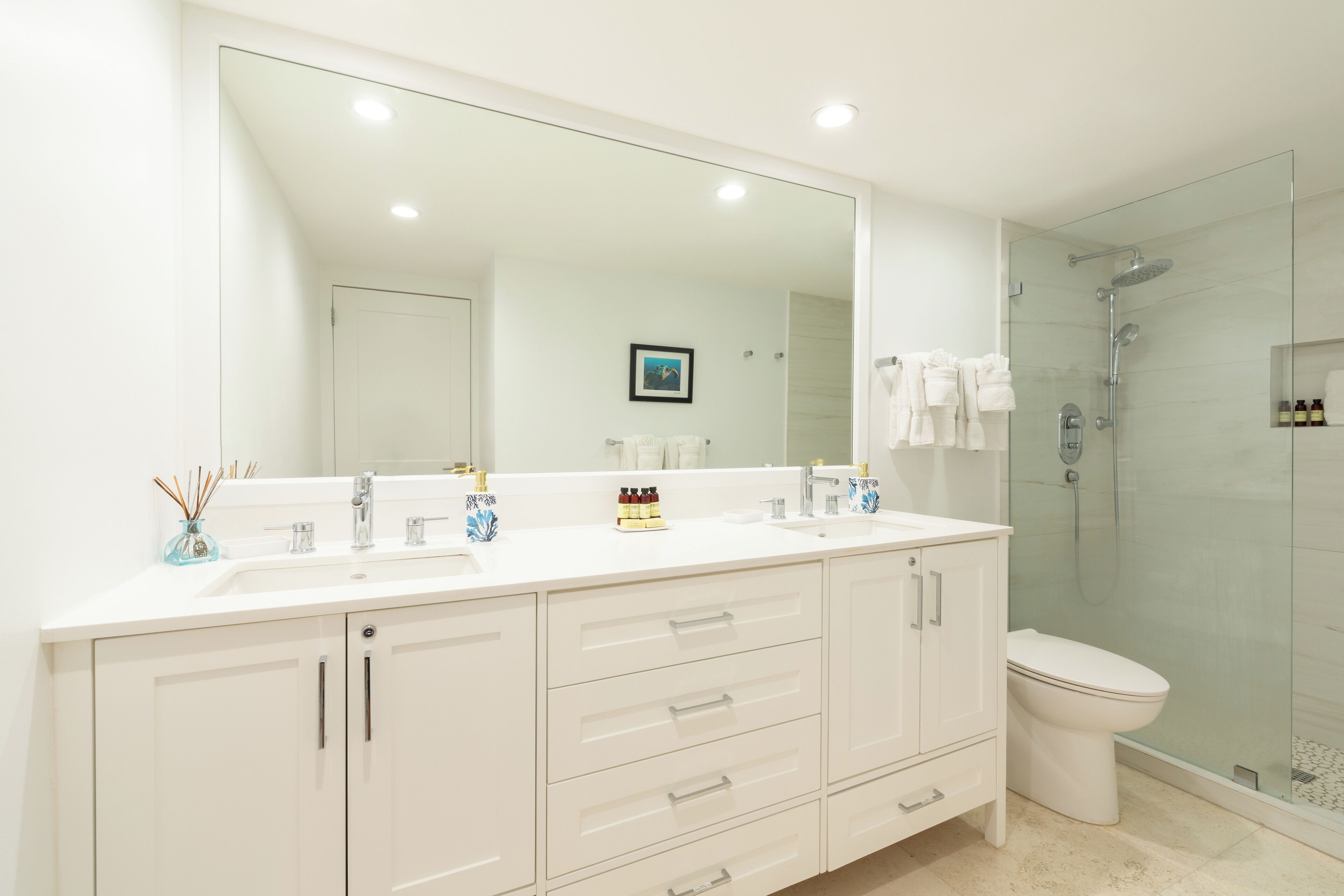 A modern bathroom with a large mirror, two sinks, a toilet, and a glass-enclosed shower.