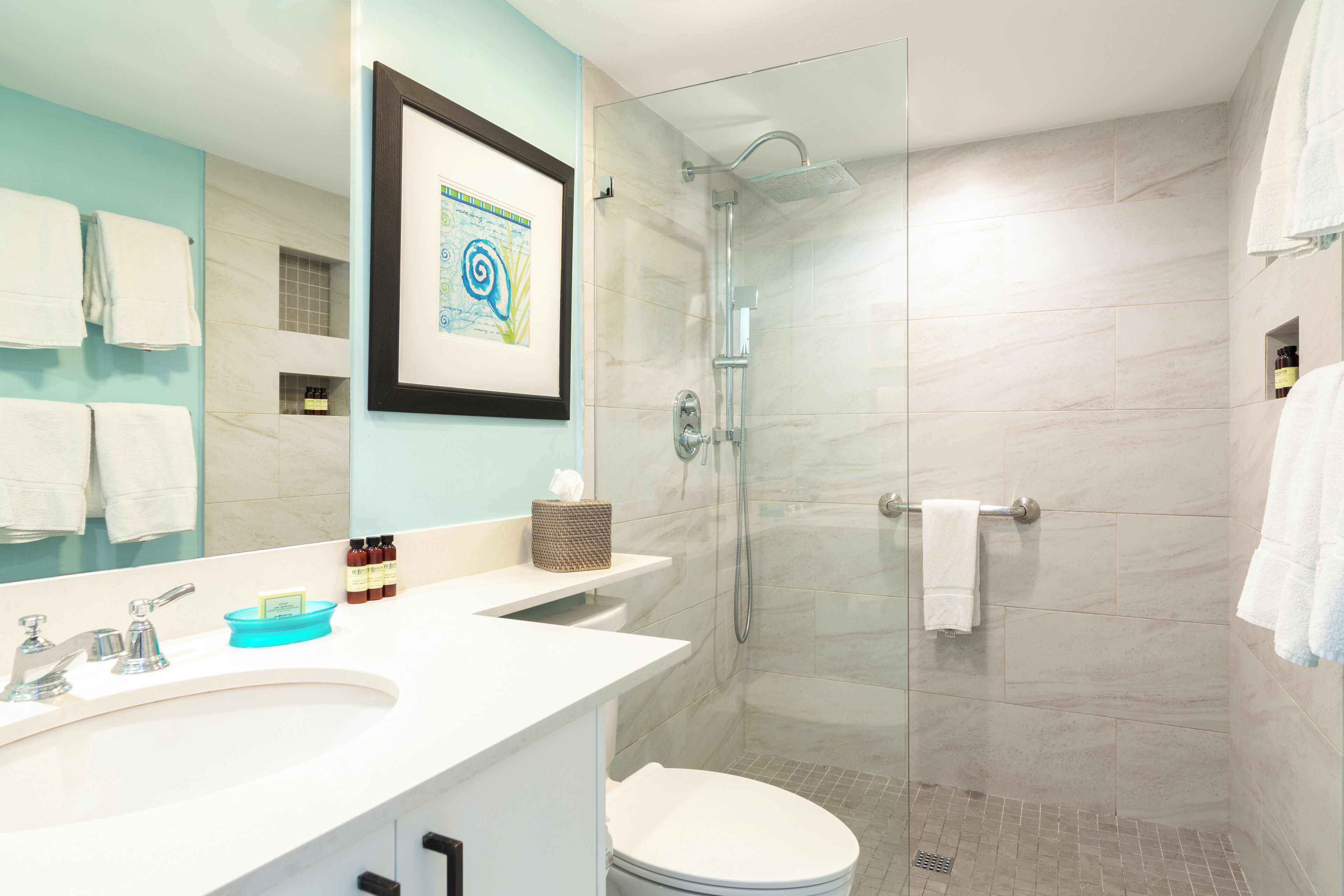 A modern bathroom with a glass-enclosed shower, a white sink with a mirror, and a framed artwork on the wall.