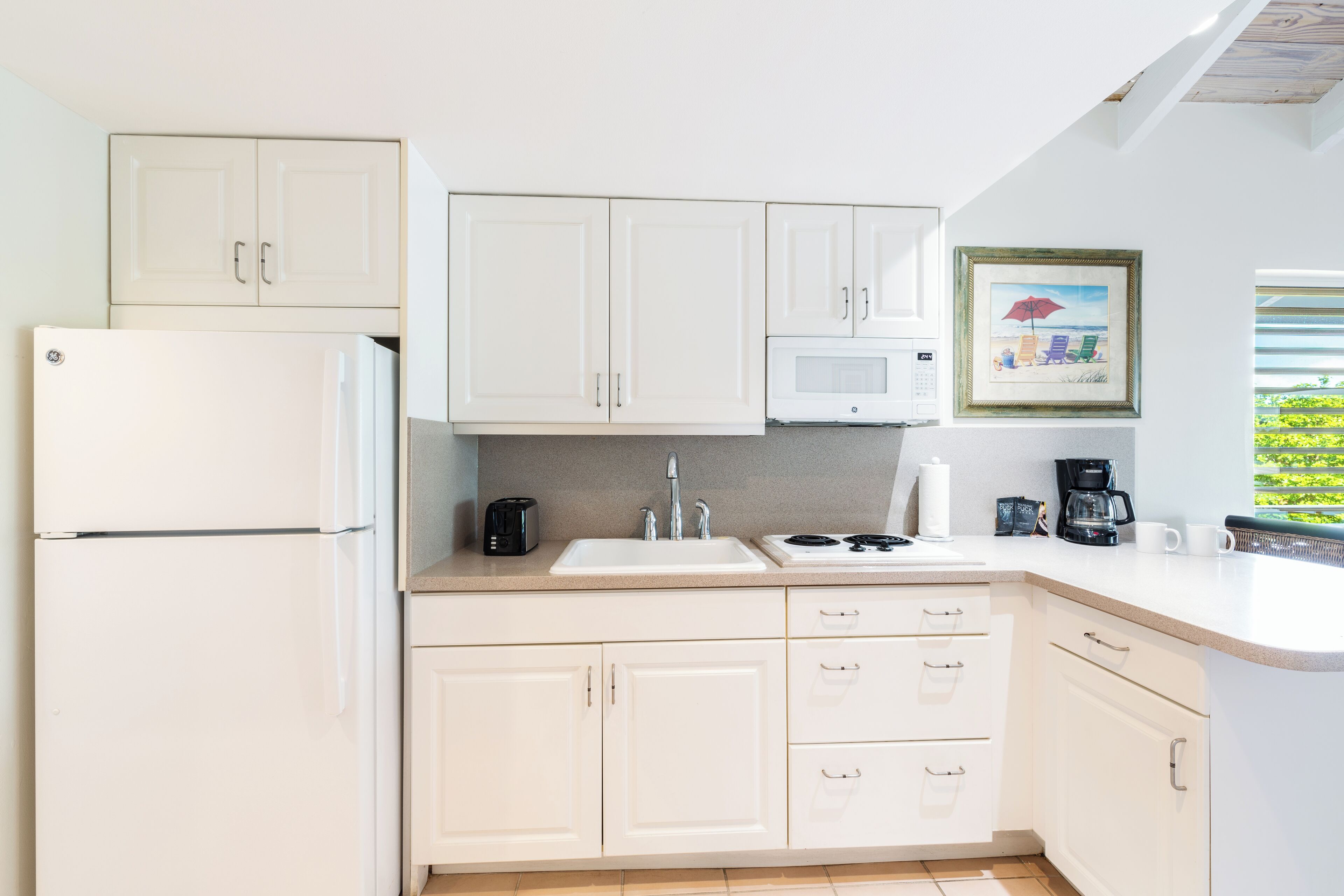 A modern kitchen with white cabinets, a refrigerator, a microwave, a sink, and a coffee maker.