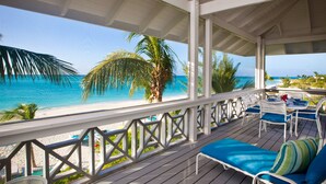 A covered outdoor area with a view of the beach and ocean. It includes a table with chairs and a lounge area with cushions. - Ocean Club East, Grace Bay Beach (Providenciales)