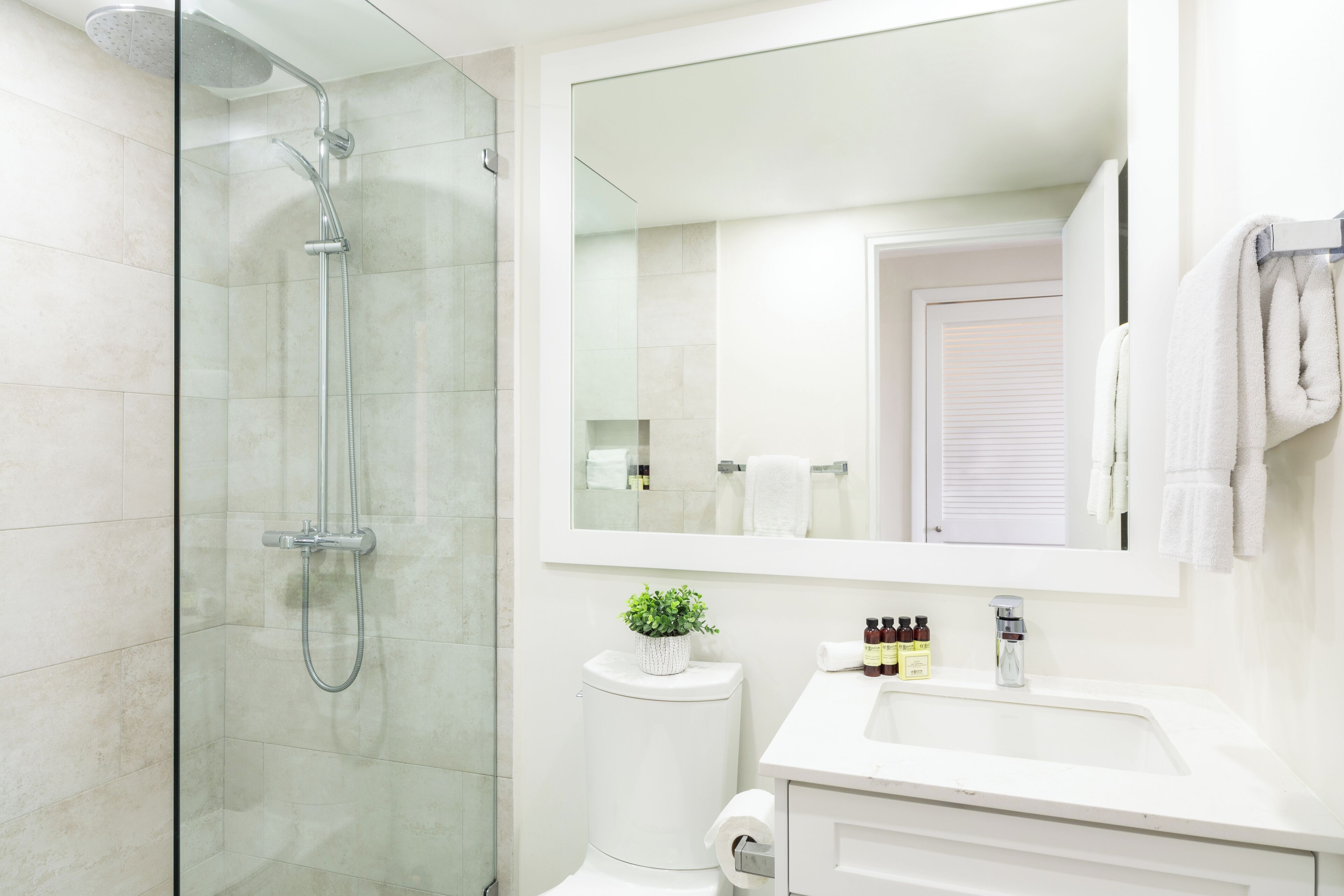 Een moderne badkamer met een douchecabine van glas, een witte wastafel, een spiegel en een toilet.