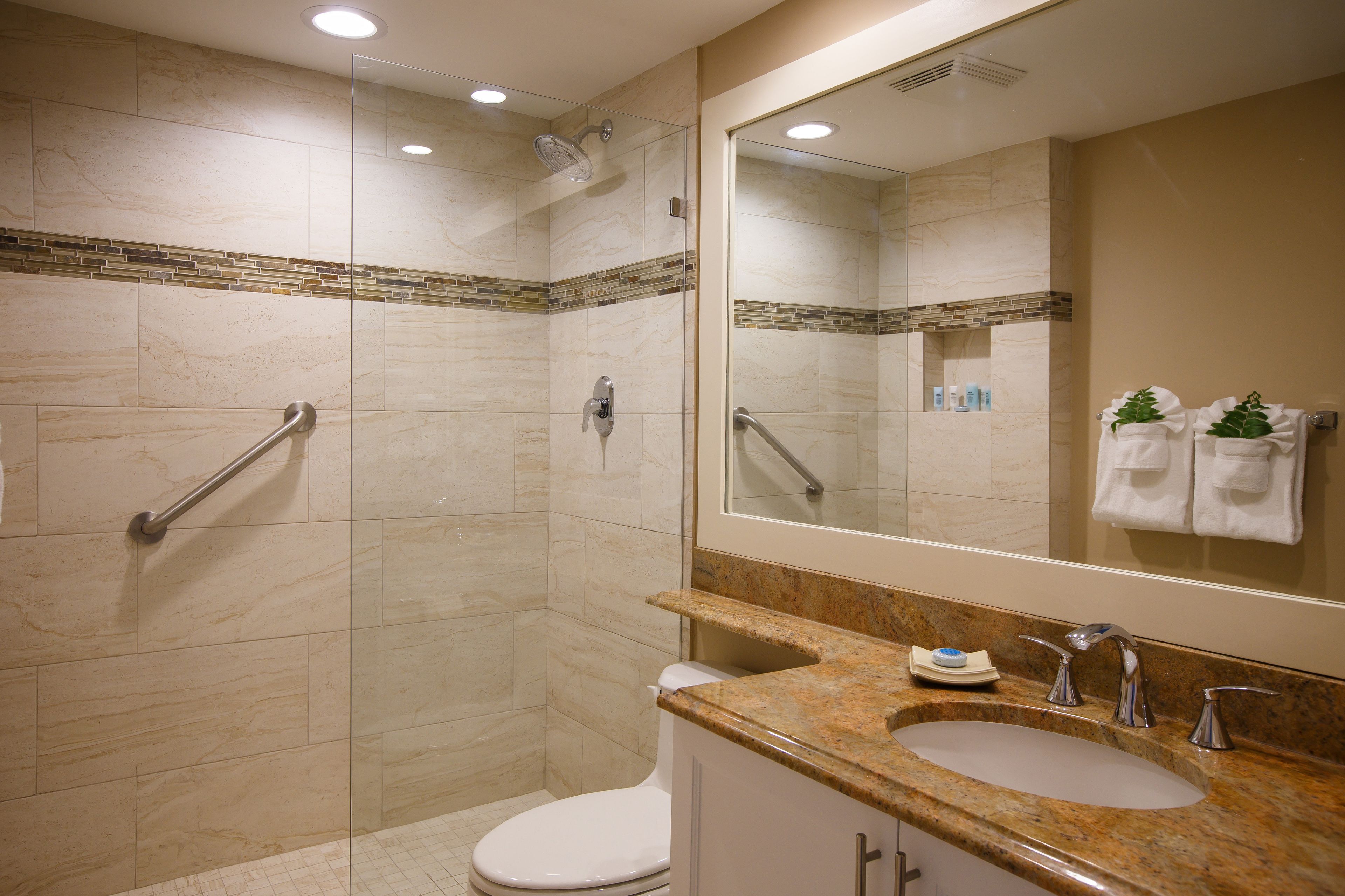 Une salle de bain moderne avec une douche à l’italienne, des toilettes, un lavabo avec un miroir et un porte-serviettes.