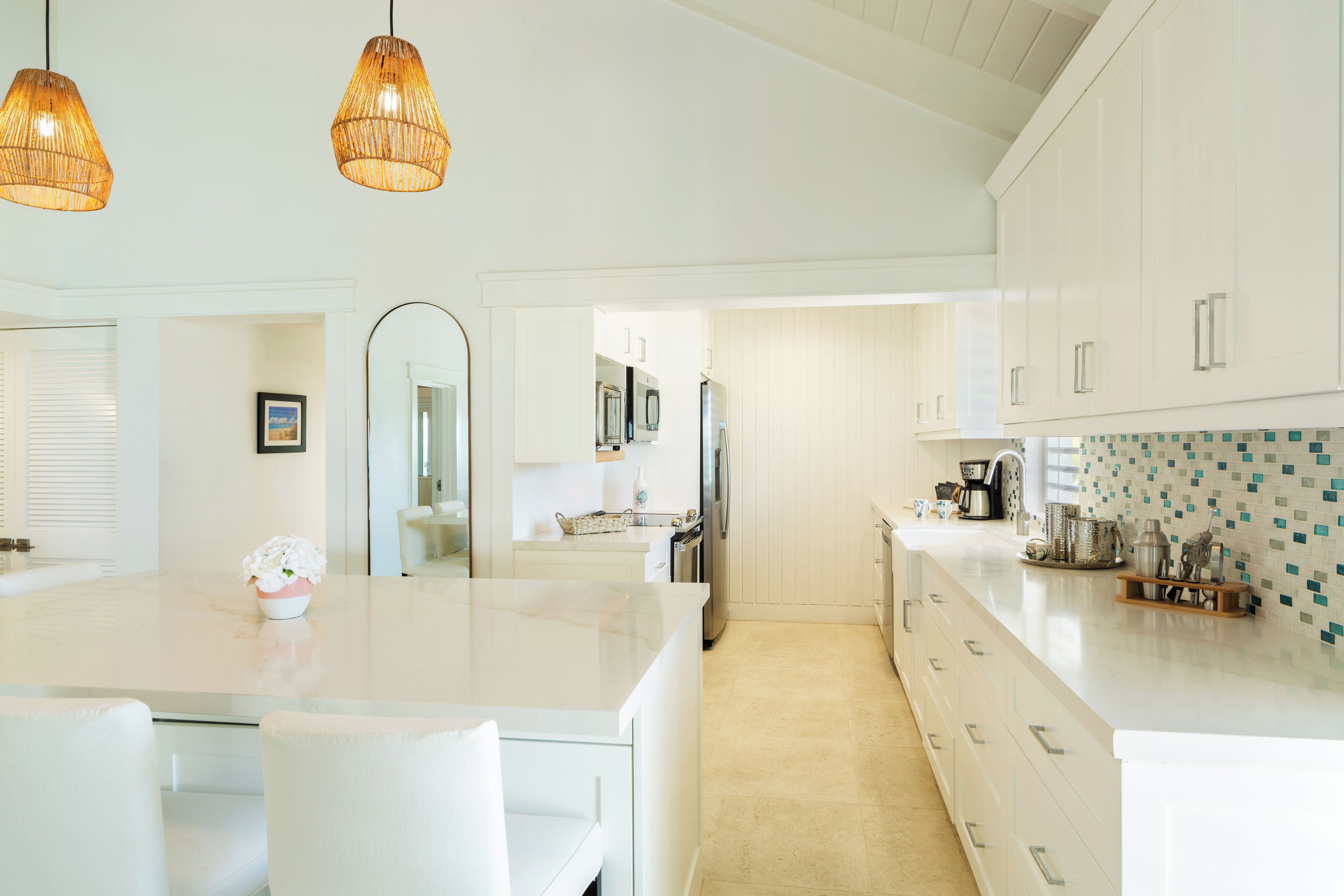 A modern kitchen with white cabinetry, a large island, and hanging wicker pendant lights.