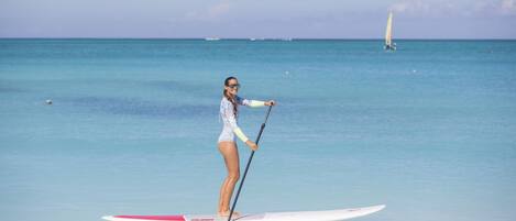 A person paddleboarding on a calm sea with a sailboat in the background.