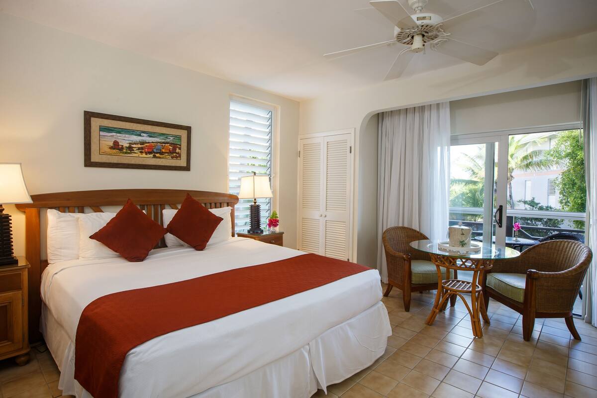 Quarto de hotel com cama, mesa redonda com cadeiras, ventoinha no teto e janela com cortinas.