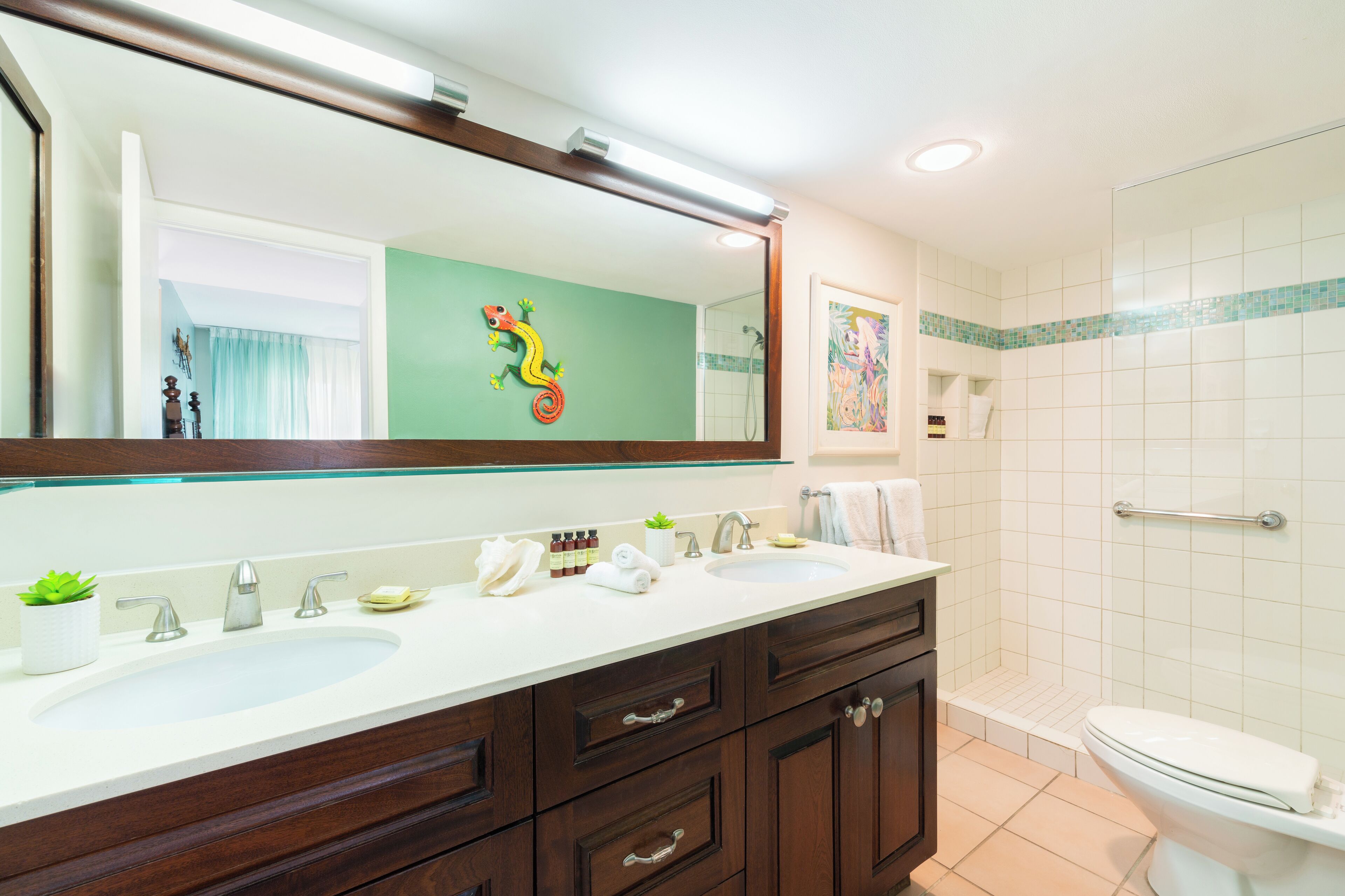 Een badkamer met een wastafelmeubel met dubbele wastafel, een grote spiegel, een douchegedeelte en een toilet.