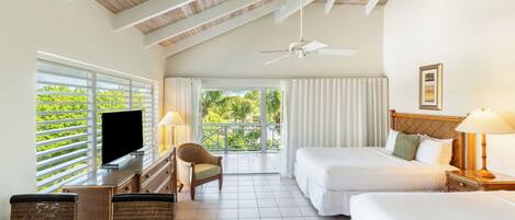 A hotel room with a large window, a ceiling fan, two beds, a TV, and a dining area with wicker furniture.