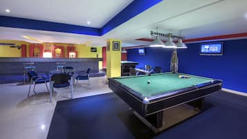 A pool table with chairs, a bar area, and a television screen in a room with blue and yellow walls.