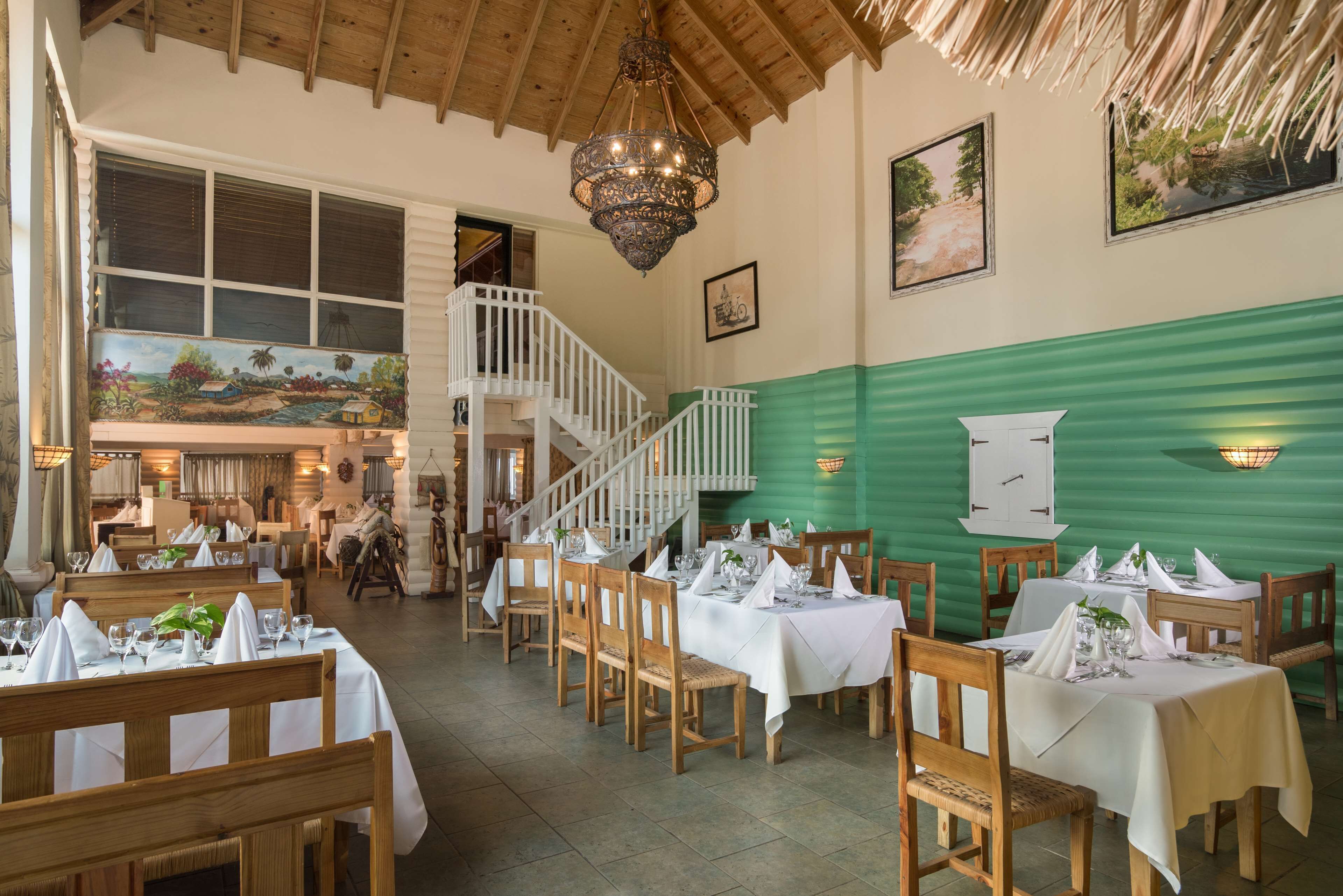 En restaurant med træborde og stole, en trappe og en grøn væg.