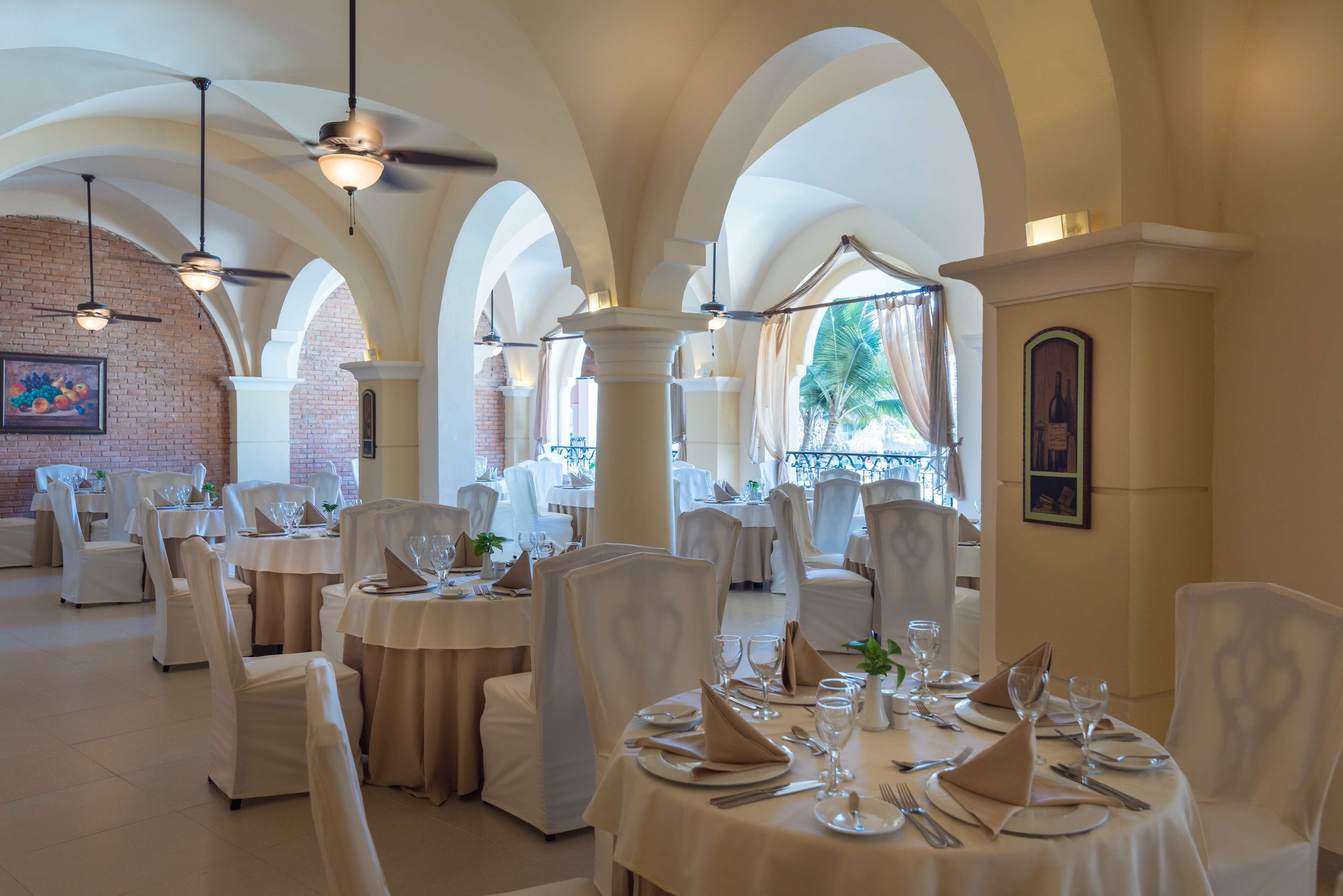A restaurant with white tablecloths, white chairs, and chandeliers.