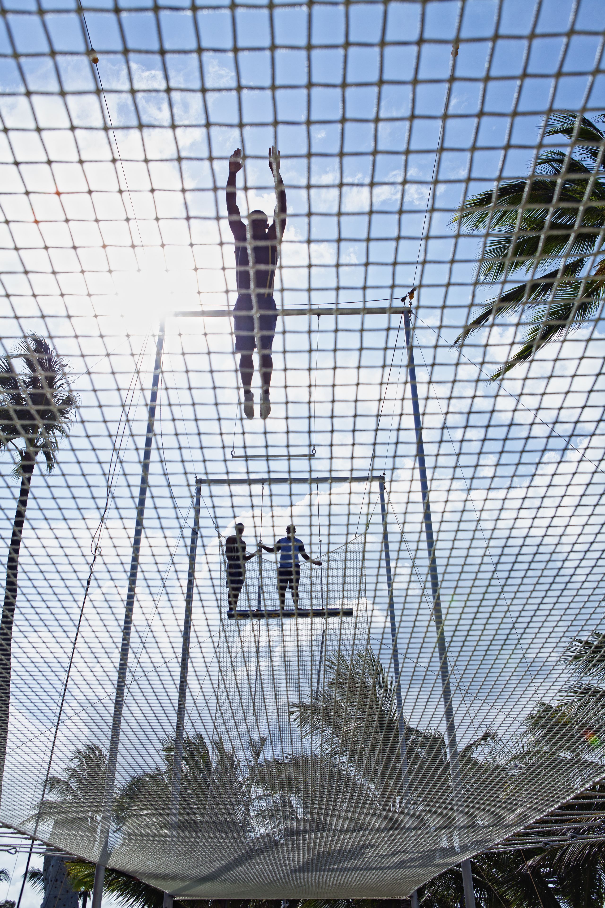 A netted structure with a person suspended in the center, another person below, and a third person standing on a platform.