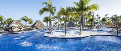 A pool area with lounge chairs, palm trees, and thatched-roof structures.