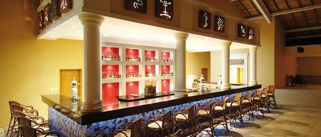 A bar area with a long counter, multiple stools, and shelves with bottles.