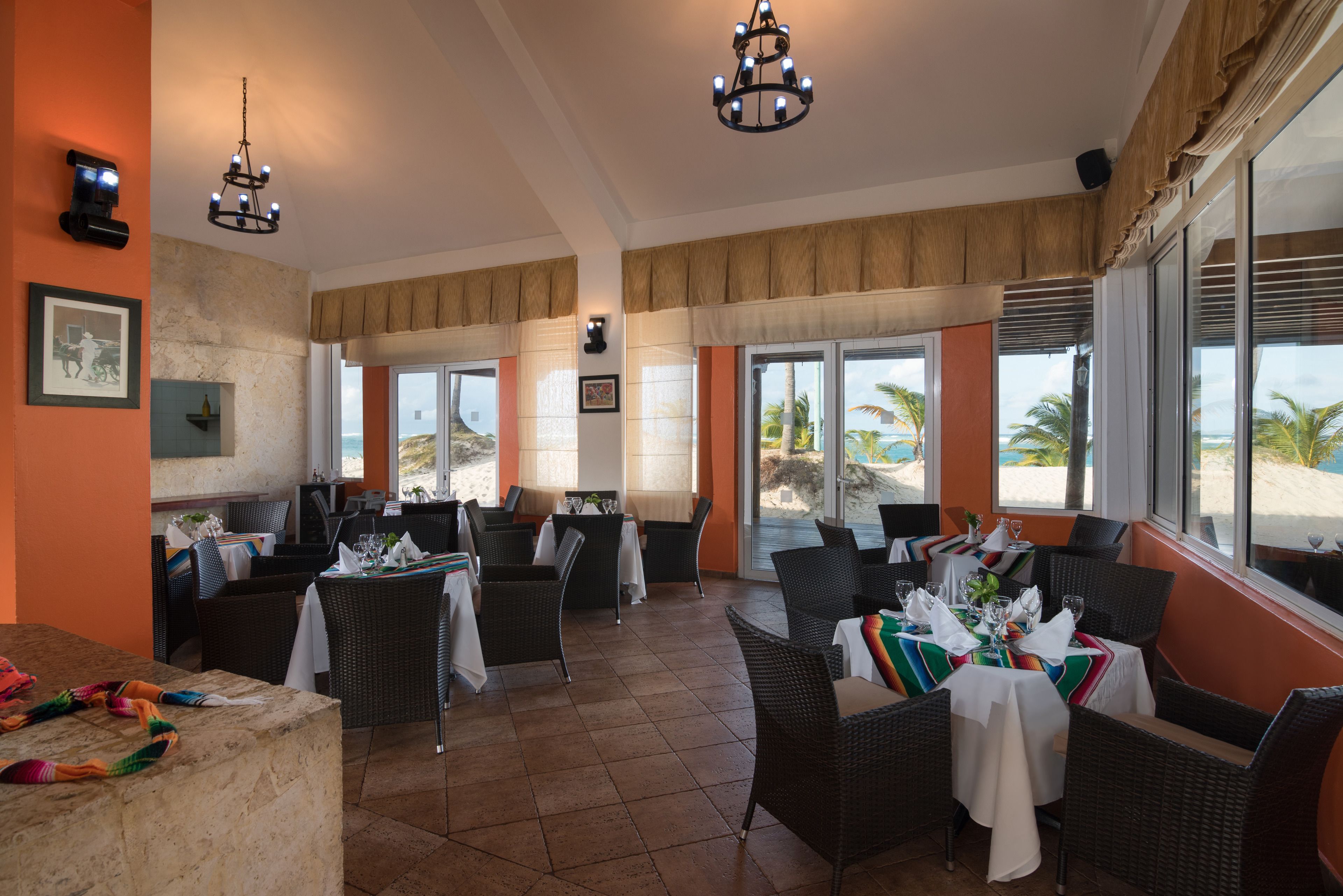 A restaurant with wicker furniture, large windows, and a view of the beach.