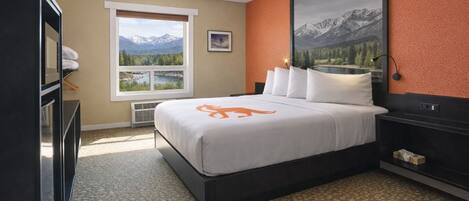 A hotel room with a bed, a dresser, a window with a mountain view, and a framed picture on the wall.