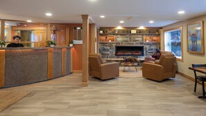 A lobby with a reception desk, seating area, stone fireplace, and artwork. - Fernie Fox Hotel (Fernie)