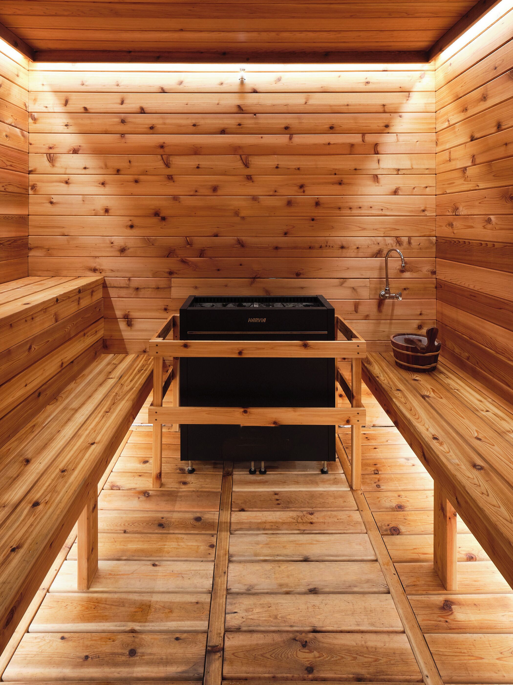 A sauna with wooden benches, a bench with a storage compartment, and a Harvia sauna heater.