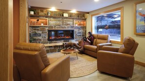 A cozy living room with a stone fireplace, leather sofas, and a large window offering a view of the outdoors. - Fernie Fox Hotel (Fernie)