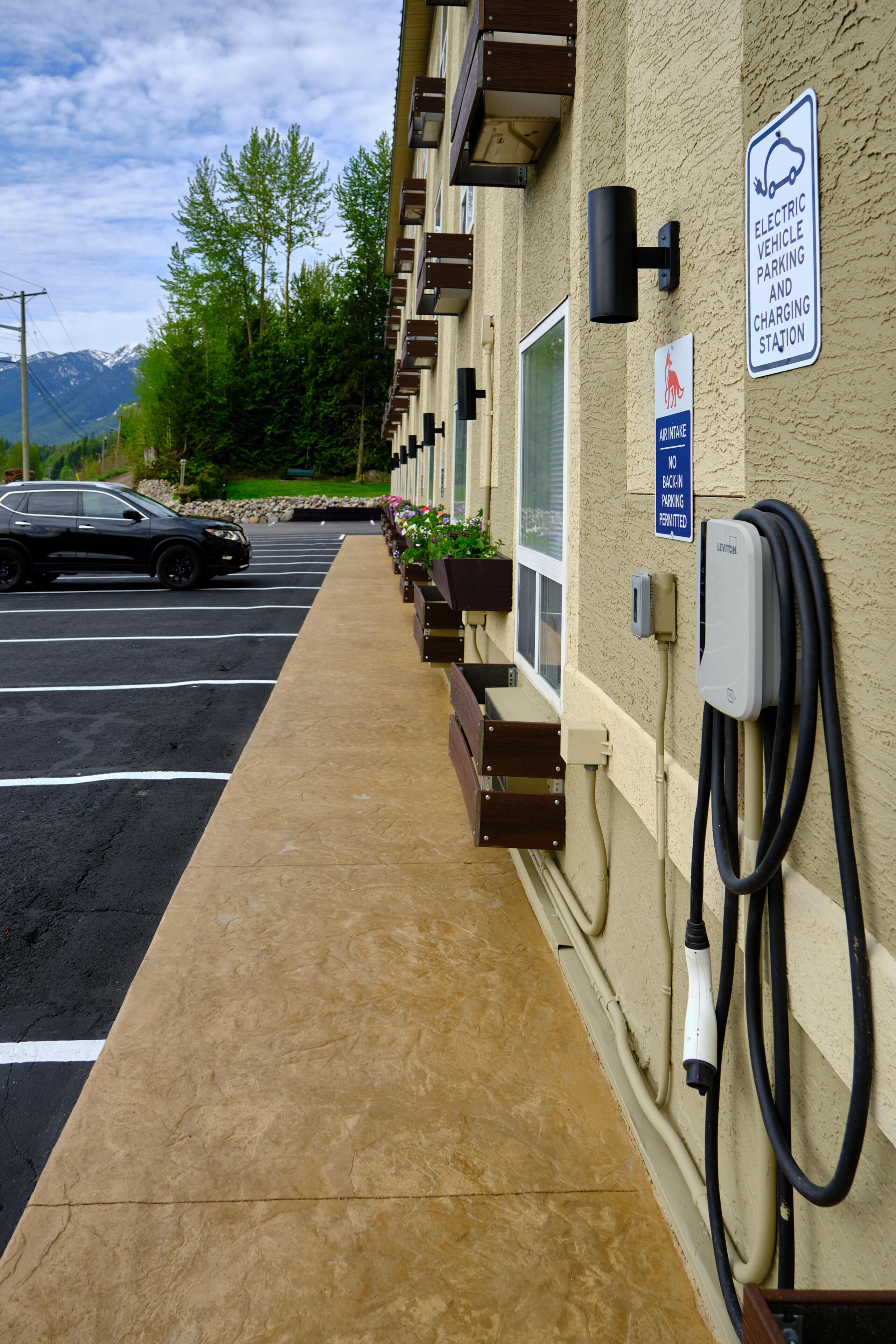 Eine Ladestation für Elektrofahrzeuge mit einem Verbotsschild für parkende Autos, einem Hydranten und einer Reihe von Fenstern an einem Gebäude.