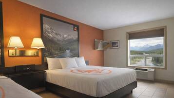 A hotel room with a bed, two bedside lamps, a large window with a mountain view, and a poster on the wall.