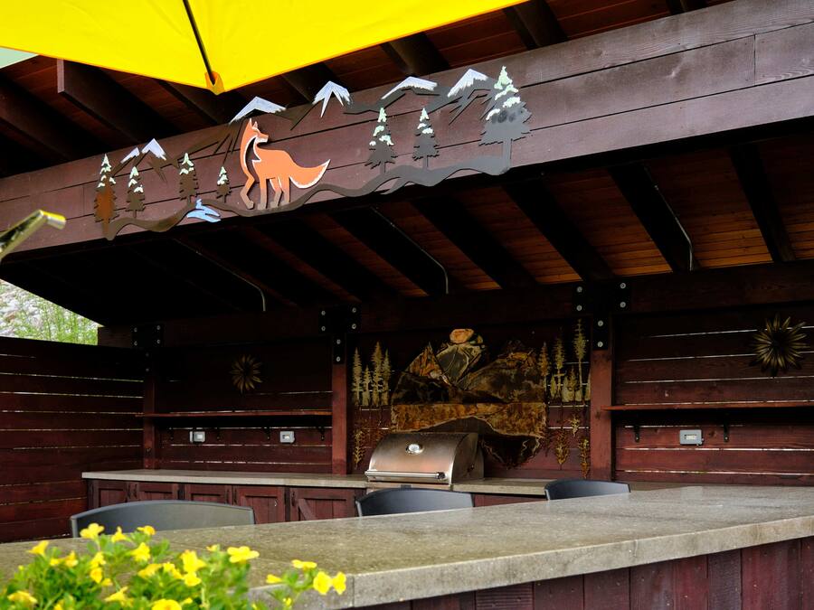 An outdoor patio with a wooden table and chairs, a grill, and a decorative mural.