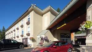 A red car parked in front of a building with a beige facade, multiple windows, and hanging flower baskets. - Fernie Fox Hotel (Fernie)