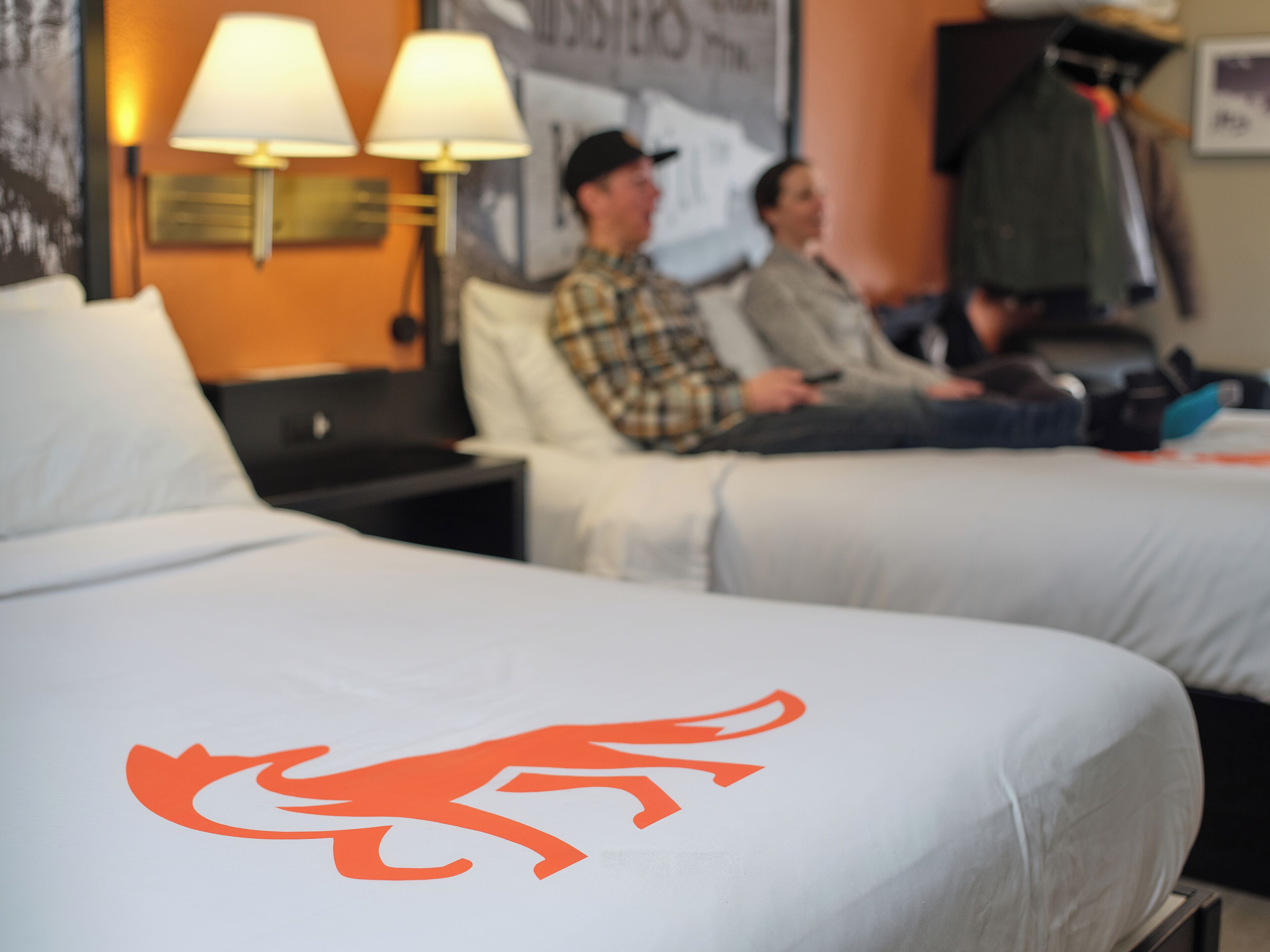 Une chambre d’hôtel avec deux lits, chacun orné d’un logo distinctif, une table de chevet et une lampe.