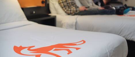 A hotel room with two beds, each with a distinct logo, a nightstand, and a lamp.